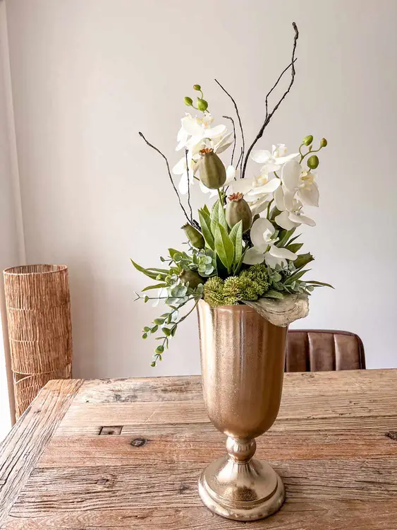 Orchideen-Arrangement in goldener Vase mit Zweigen und Grün